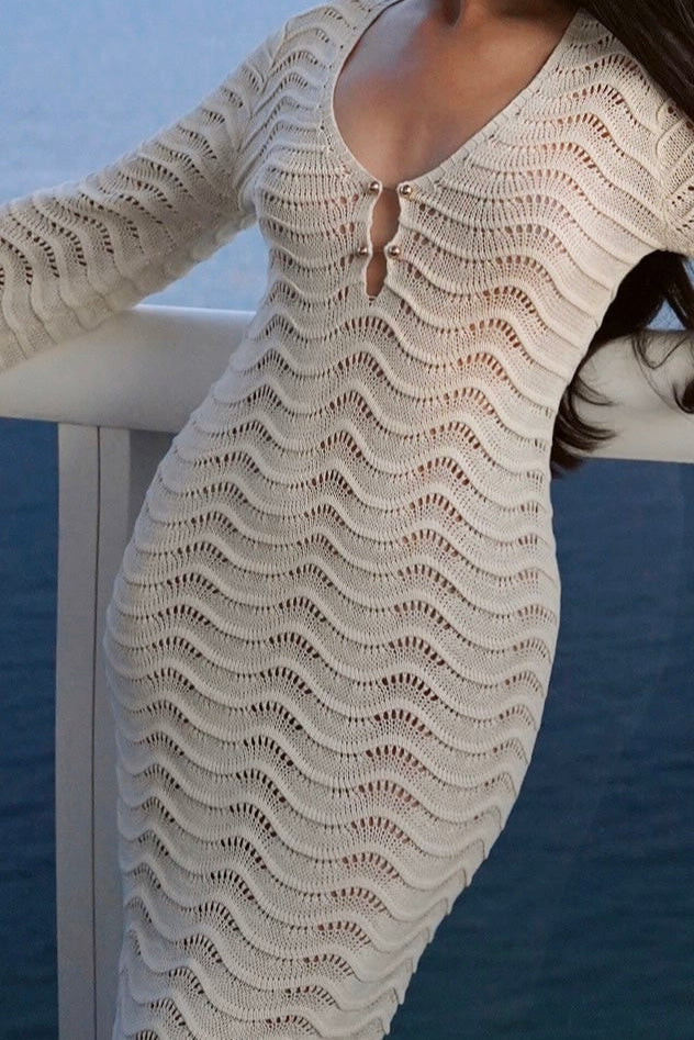 Woman in a beige crochet dress standing on a balcony with ocean view